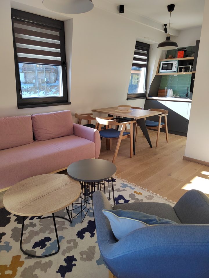 Roze sofa i klub stolići, u pozadini trpezarija